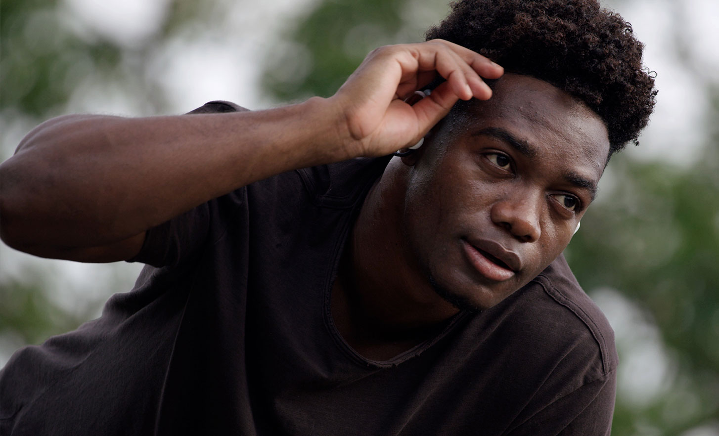 Gambar seorang pria di luar ruang sedang menyentuh dahi dan mengenakan headphone Float Run Sony