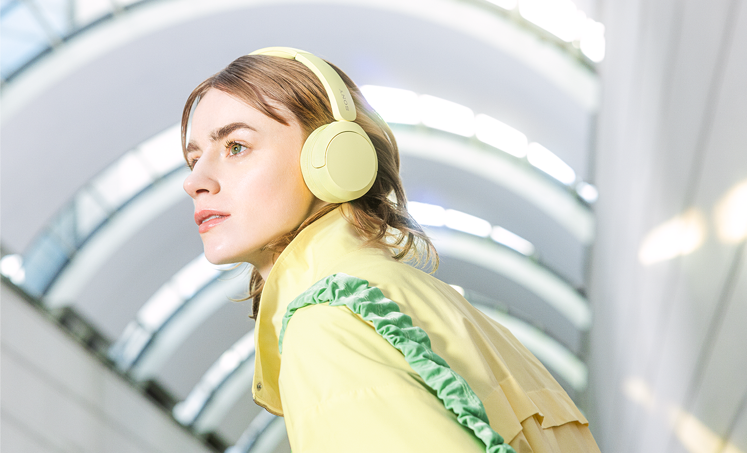 Orang yang mengenakan sepasang headphone Sony WH-CH520 berwarna kuning dengan jaket modis yang serasi.